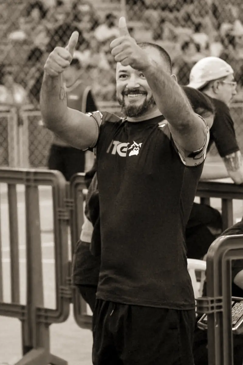 Pécora de rash guard, sorrindo e com os dois polegares para cima no ginásio da competição
