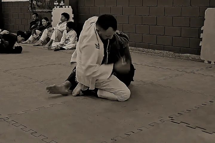 Treino de jiu-jitsu no tatame, com crianças de kimono assistindo