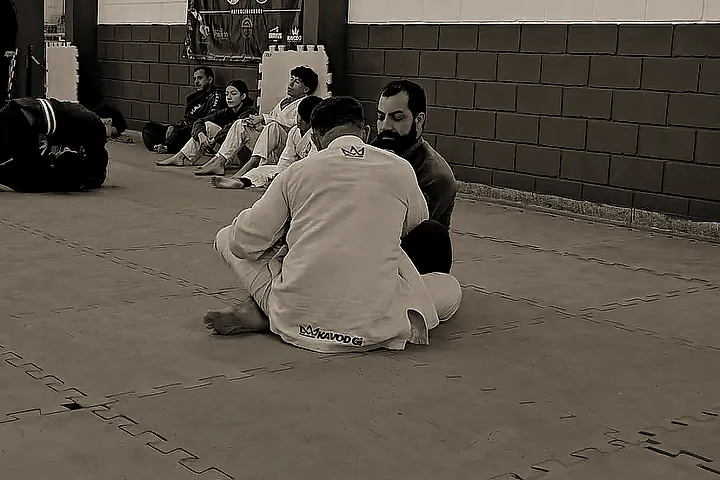 Treino de jiu-jitsu, com crianças de kimono sentadas na beira do tatame